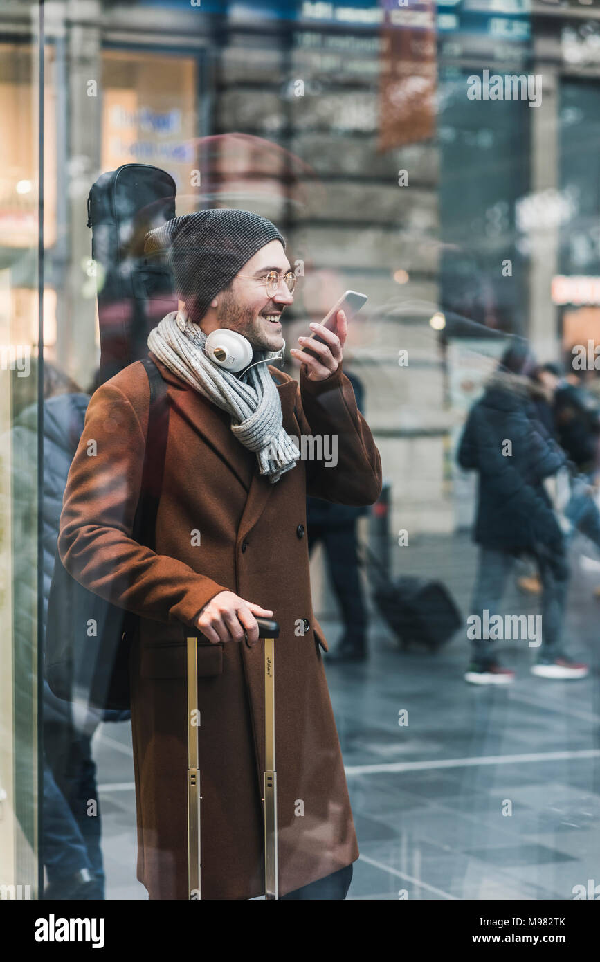 Smiling Young man with guitar case à la station using cell phone Banque D'Images
