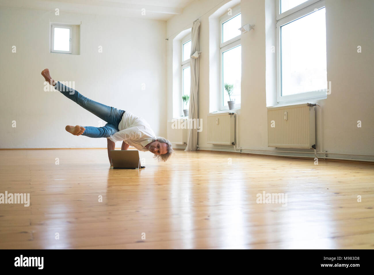 Man doing a handstand in empty room looking at tablet Banque D'Images
