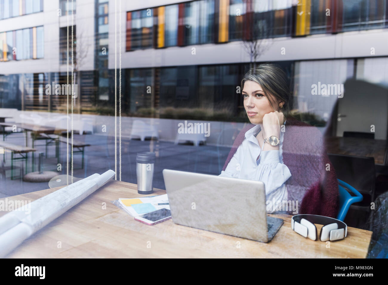 Jeune femme avec un ordinateur portable et documents derrière la vitre Banque D'Images