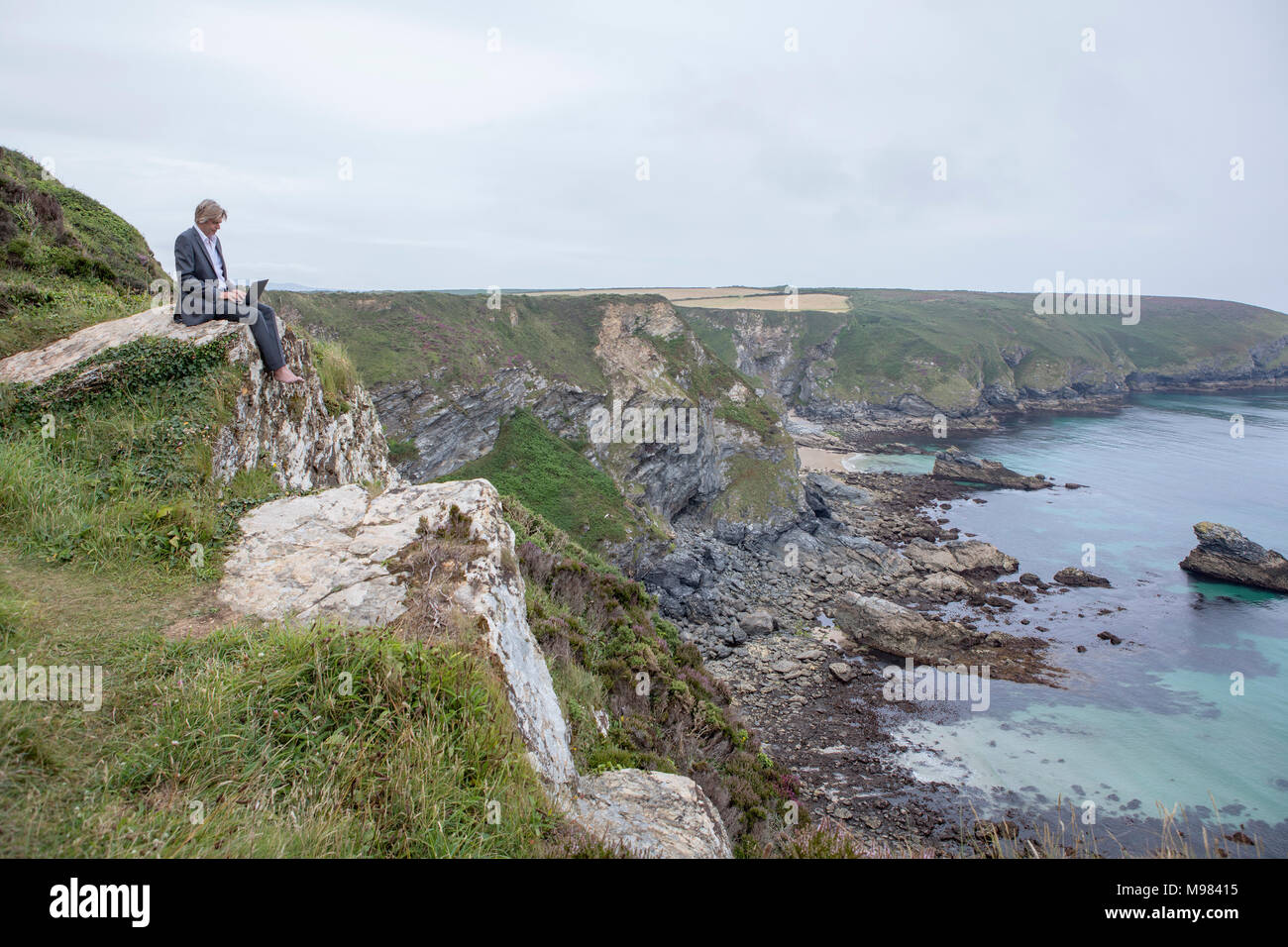 UK, Cornwall, Gwithian, businessman sitting at the coast using laptop Banque D'Images