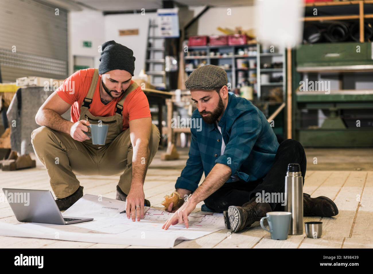 Deux hommes avec un ordinateur portable à la recherche au plan de la construction sur le sol Banque D'Images