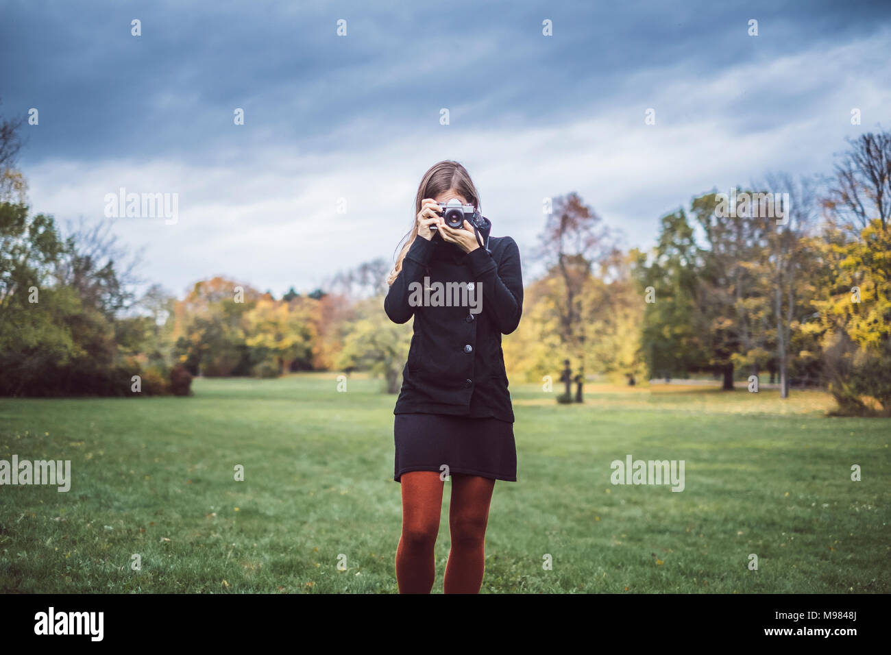 Jeune femme à prendre des photos avec l'appareil photo sur une prairie de autumnal park Banque D'Images