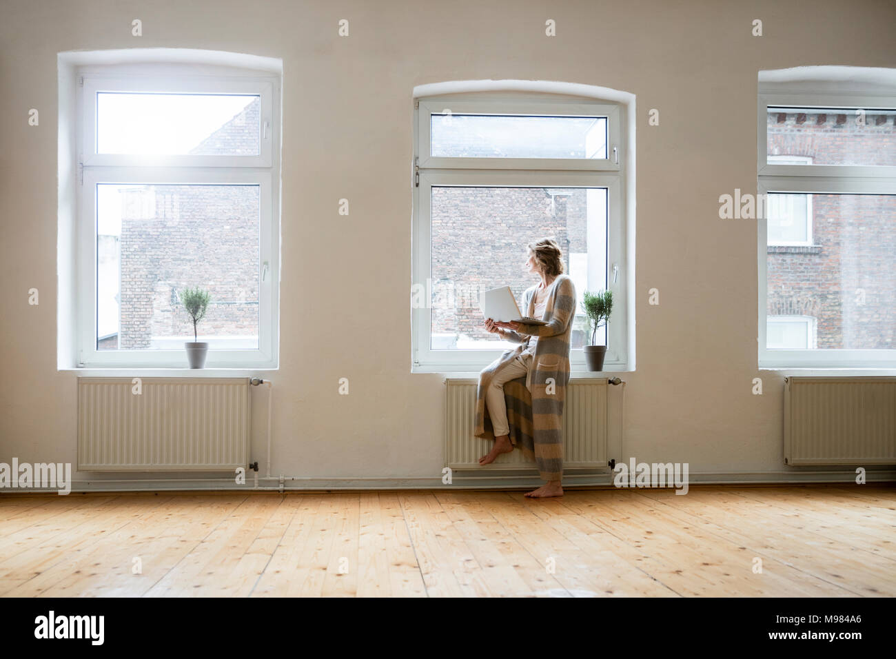 Mature Woman in empty room holding laptop à la fenêtre Banque D'Images