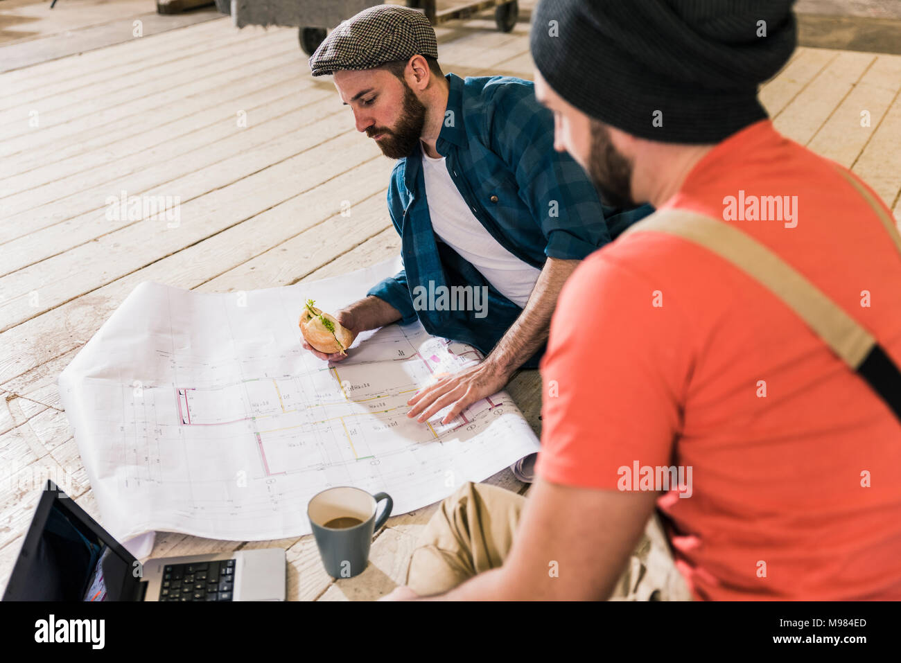 Deux hommes avec un ordinateur portable à la recherche au plan de la construction sur le sol Banque D'Images
