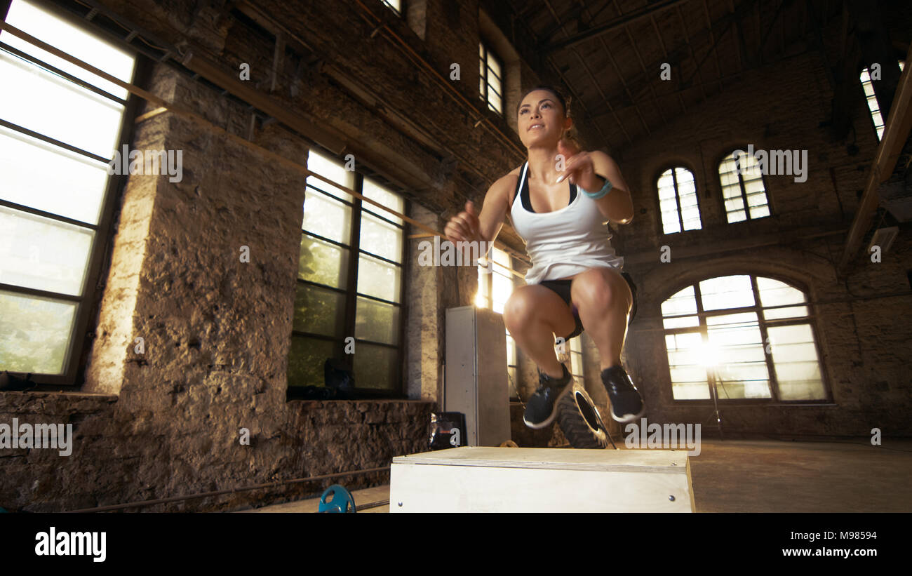 Mettre en place n'femme athlétique fort sauts dans l'usine déserte de sport. L'exercice intense est une partie de son programme de formation de remise en forme Croix quotidienne. Banque D'Images