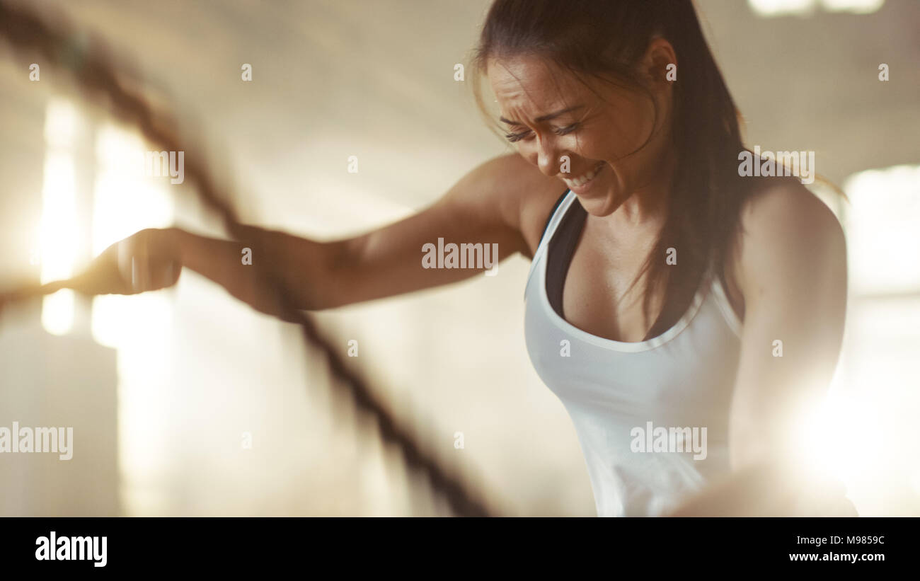 Femme athlétique dans un Gym Exercices avec des cordes de bataille lors de son contre Fitness Workout/ la formation d'intervalle de haute intensité. Elle est en sueur et musculaire Banque D'Images