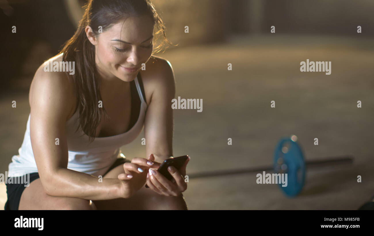 Belle Brunette athlétique Smartphone utilise alors qu'elle repose sur le banc après sa Croix Salle de Sport fitness musculation intensive de formation. Banque D'Images