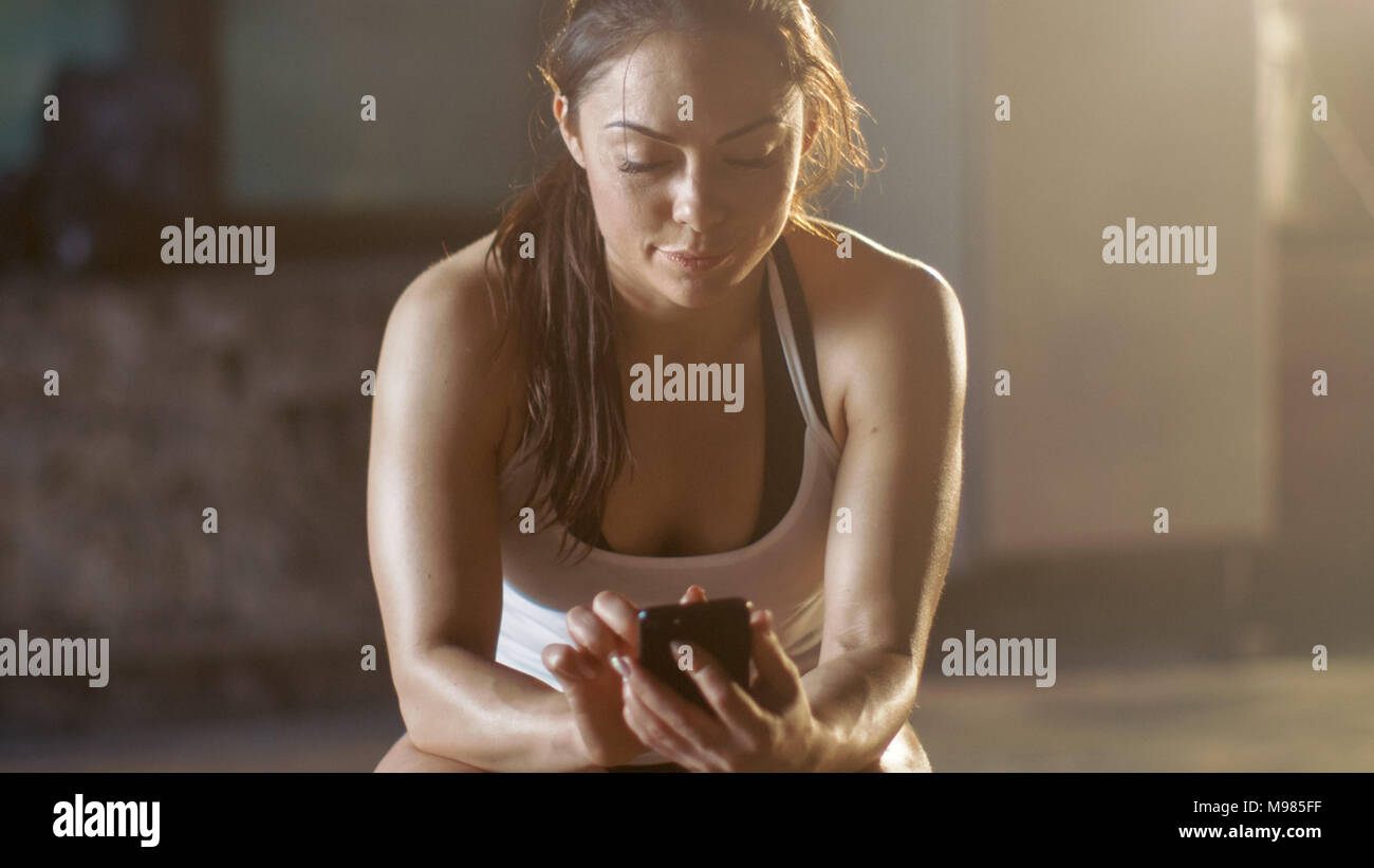 Belle Brunette athlétique Smartphone utilise alors qu'elle repose sur le banc après sa Croix Salle de Sport fitness musculation intensive de formation. Banque D'Images
