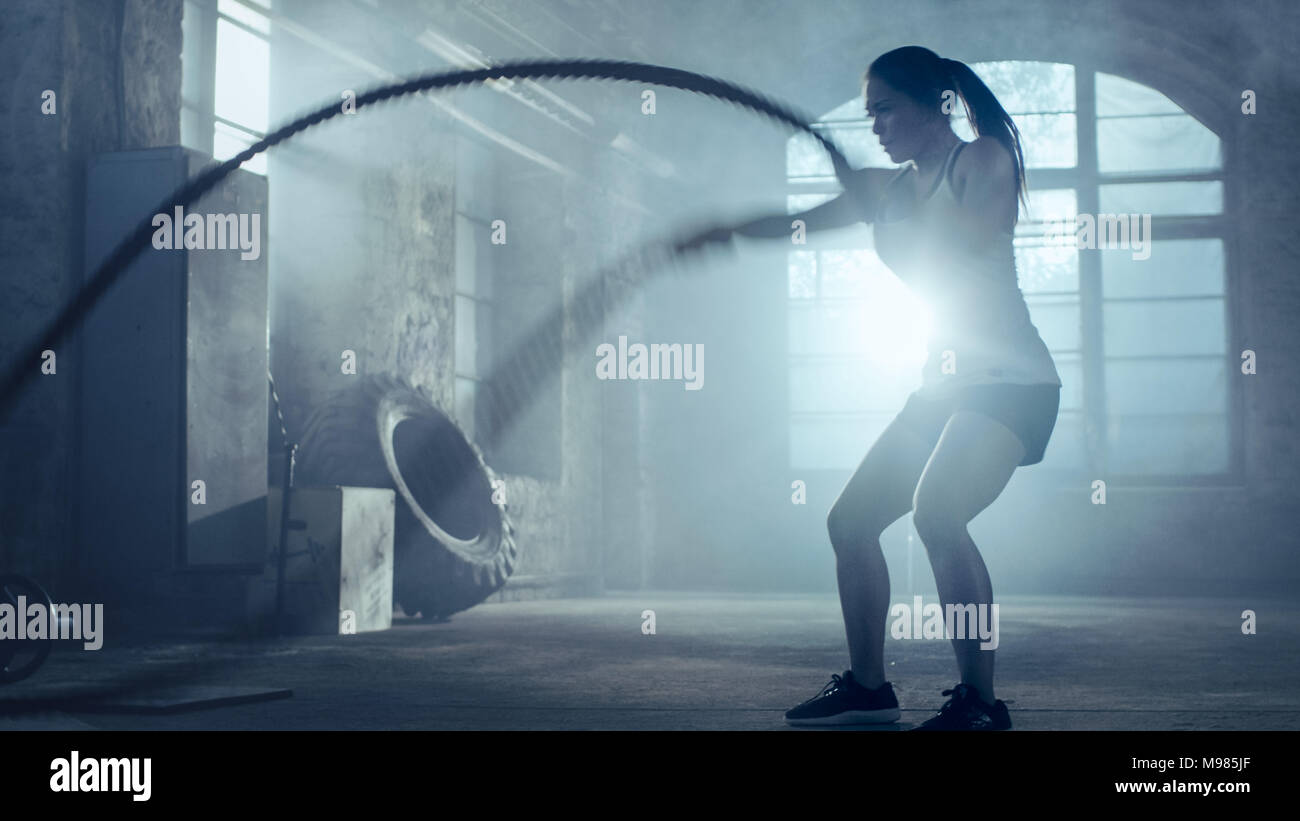 Femme athlétique solide des exercices avec des cordes de bataille dans le cadre de sa routine d'entraînement de sport de remise en forme. Elle est tout en sueur Banque D'Images