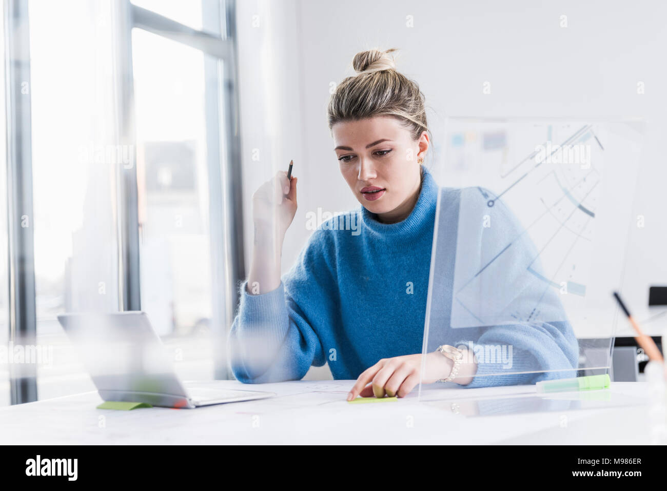 Young woman with laptop design transparent et travaillant sur le plan at desk in office Banque D'Images