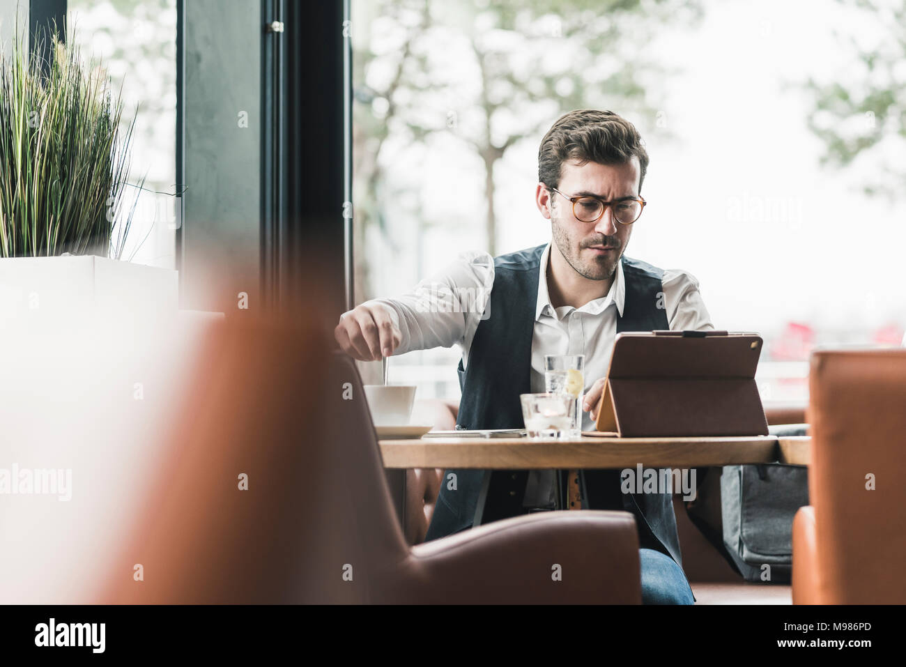 Jeune homme à l'aide de comprimé à la fenêtre dans un café Banque D'Images