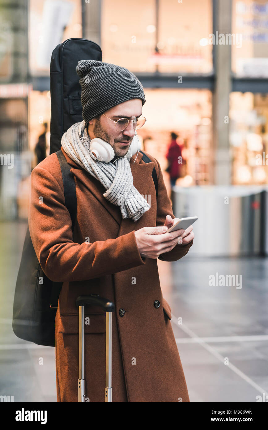 Jeune homme à l'étui à guitare using cell phone Banque D'Images