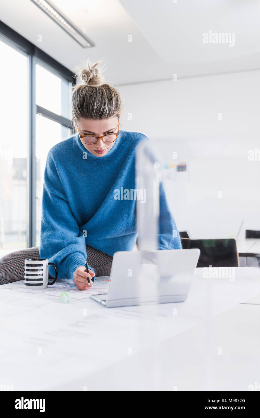 Jeune femme avec un ordinateur portable et le plan working at desk in office Banque D'Images