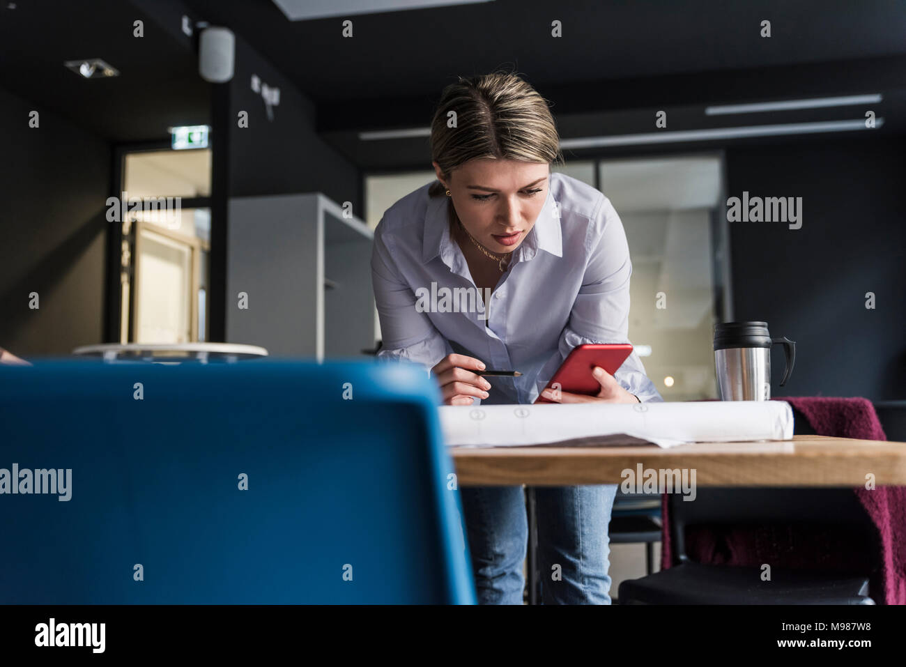 Young woman with cell phone et le plan de la table in office Banque D'Images