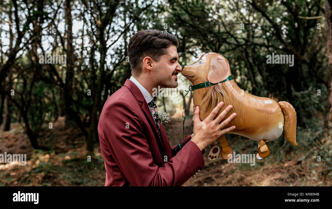 Homme portant costume dans forêt jouant avec drôle ballon en forme de chien Banque D'Images