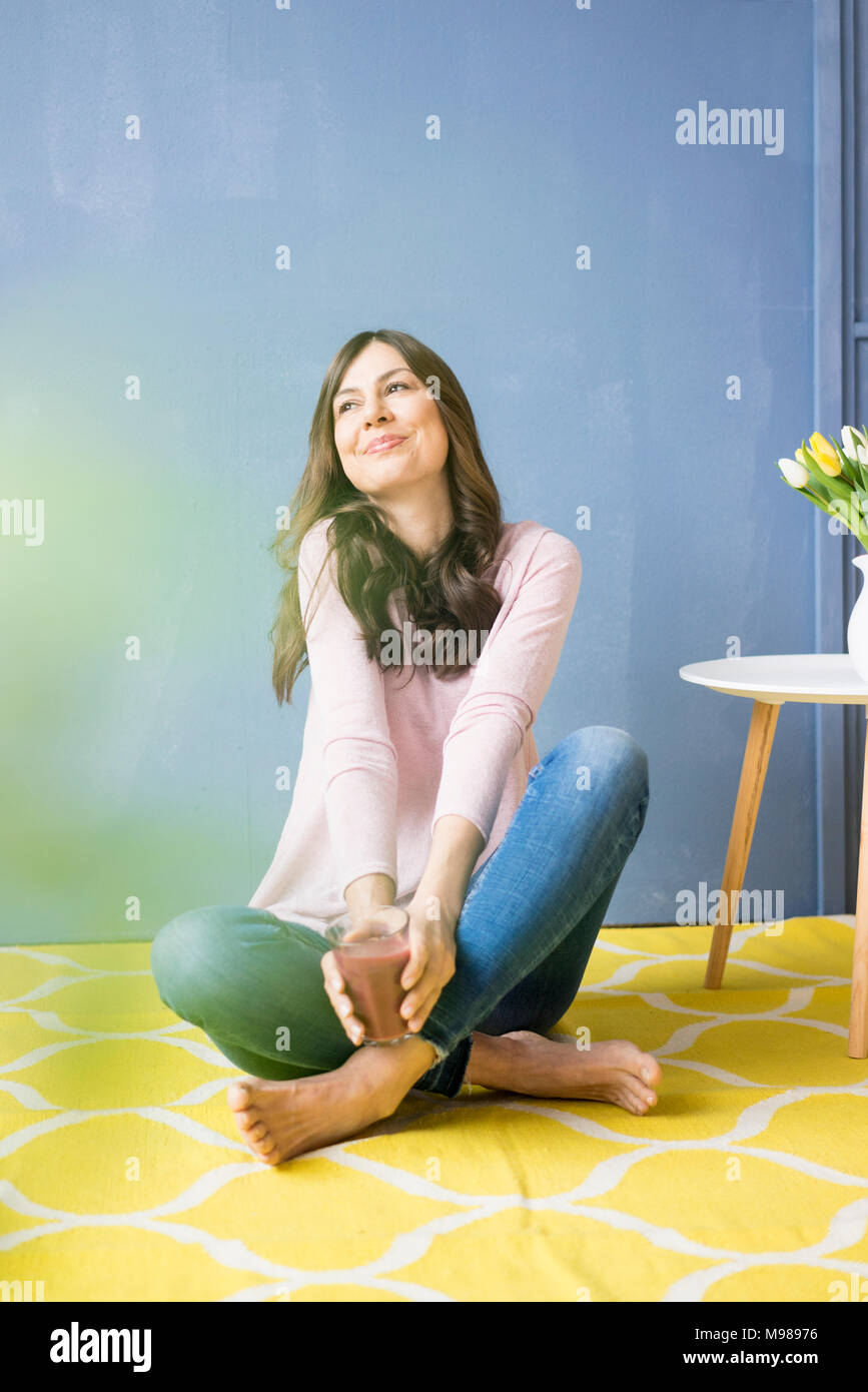 Smiling woman sitting on floor holding verre de jus Banque D'Images