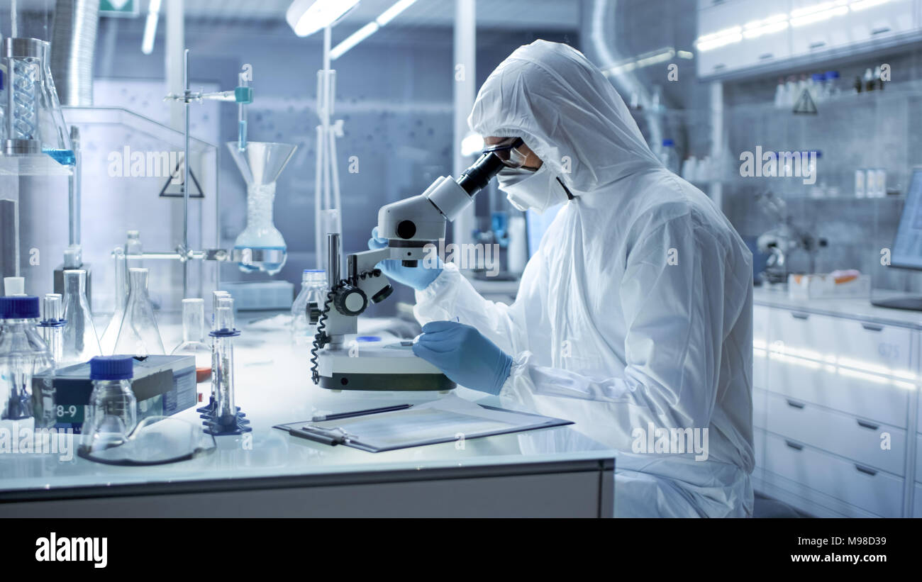 Dans un laboratoire de recherche de haut niveau scientifique dans une combinaison de Petri examine au microscope. Banque D'Images