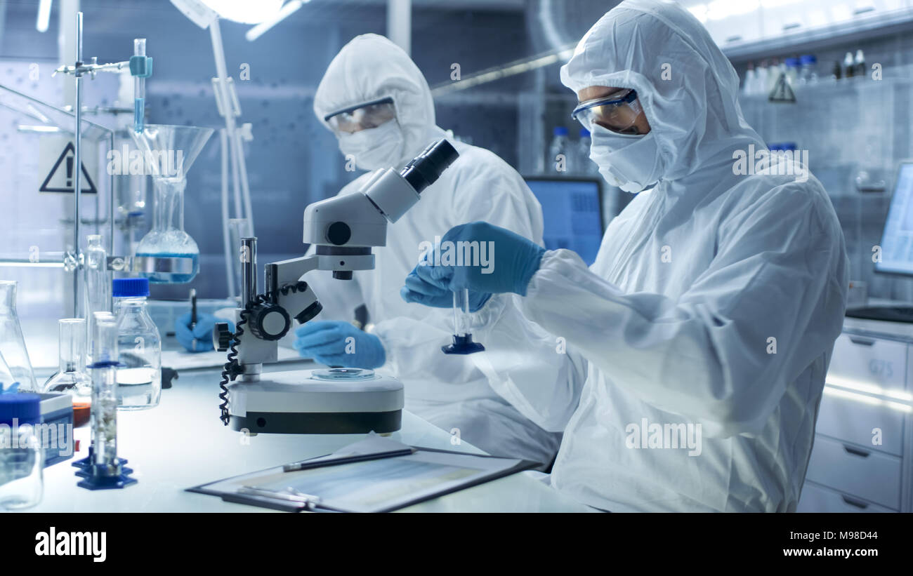 Dans un laboratoire de haut niveau des scientifiques dans une combinaison d'une recherche. Pharmacie des échantillons et ajuste son collègue consigne les résultats. Banque D'Images
