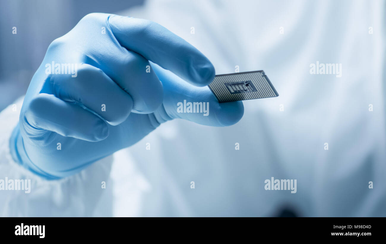 Dans l'usine ultra moderne de fabrication électronique Ingénieur de conception en combinaison stérile avec des gants et de Microchip détient l'examine. Banque D'Images