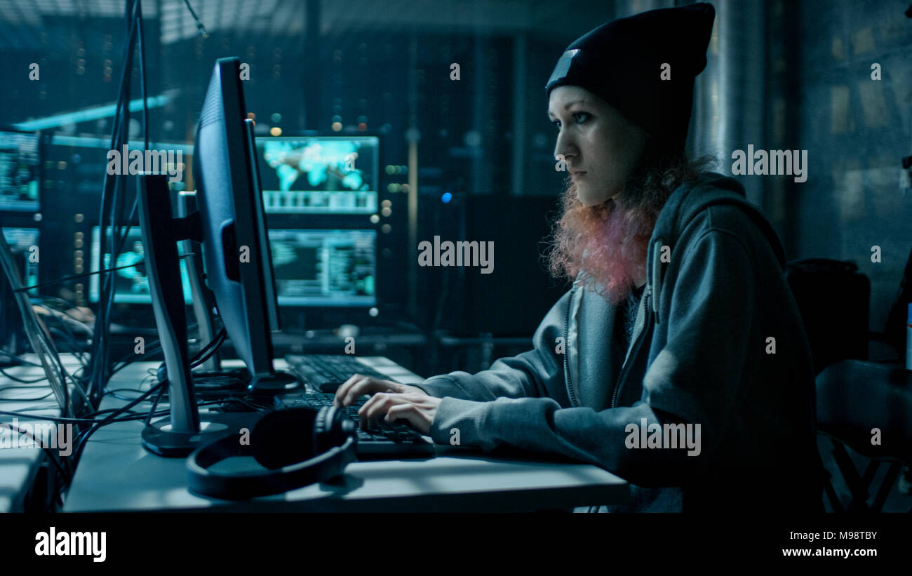 Teenage Girl pirate non-conformiste à l'aide d'ordinateur pour attaquer les serveurs d'entreprise avec des logiciels malveillants. Chambre est sombre, le néon et a beaucoup d'Affichages. Banque D'Images