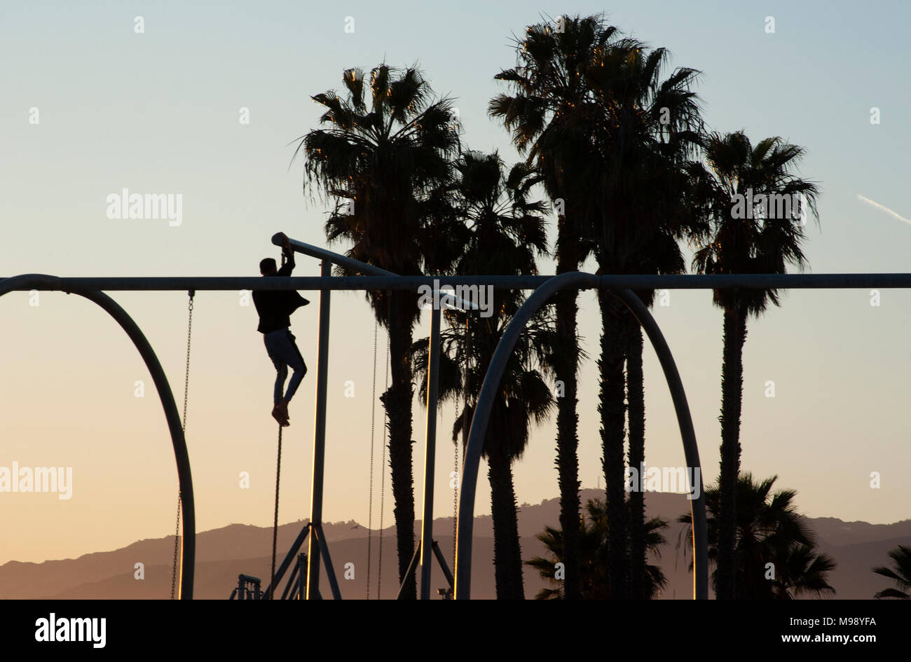 Man climbing pôle à jeux pour enfants sur la plage de Santa Monica à Los Angeles, CA Banque D'Images