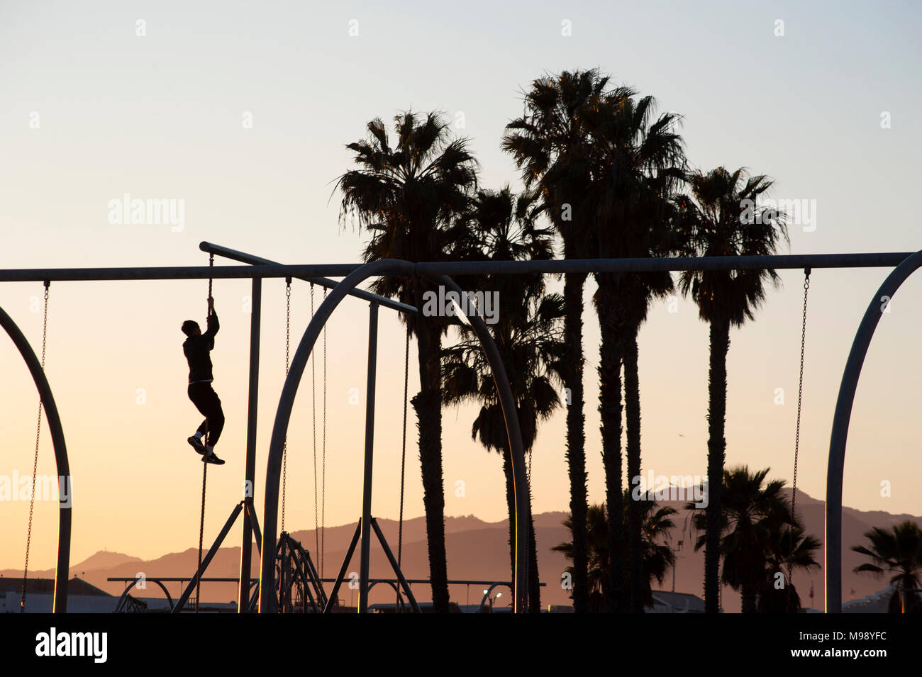 Man climbing pôle à jeux pour enfants sur la plage de Santa Monica à Los Angeles, CA Banque D'Images