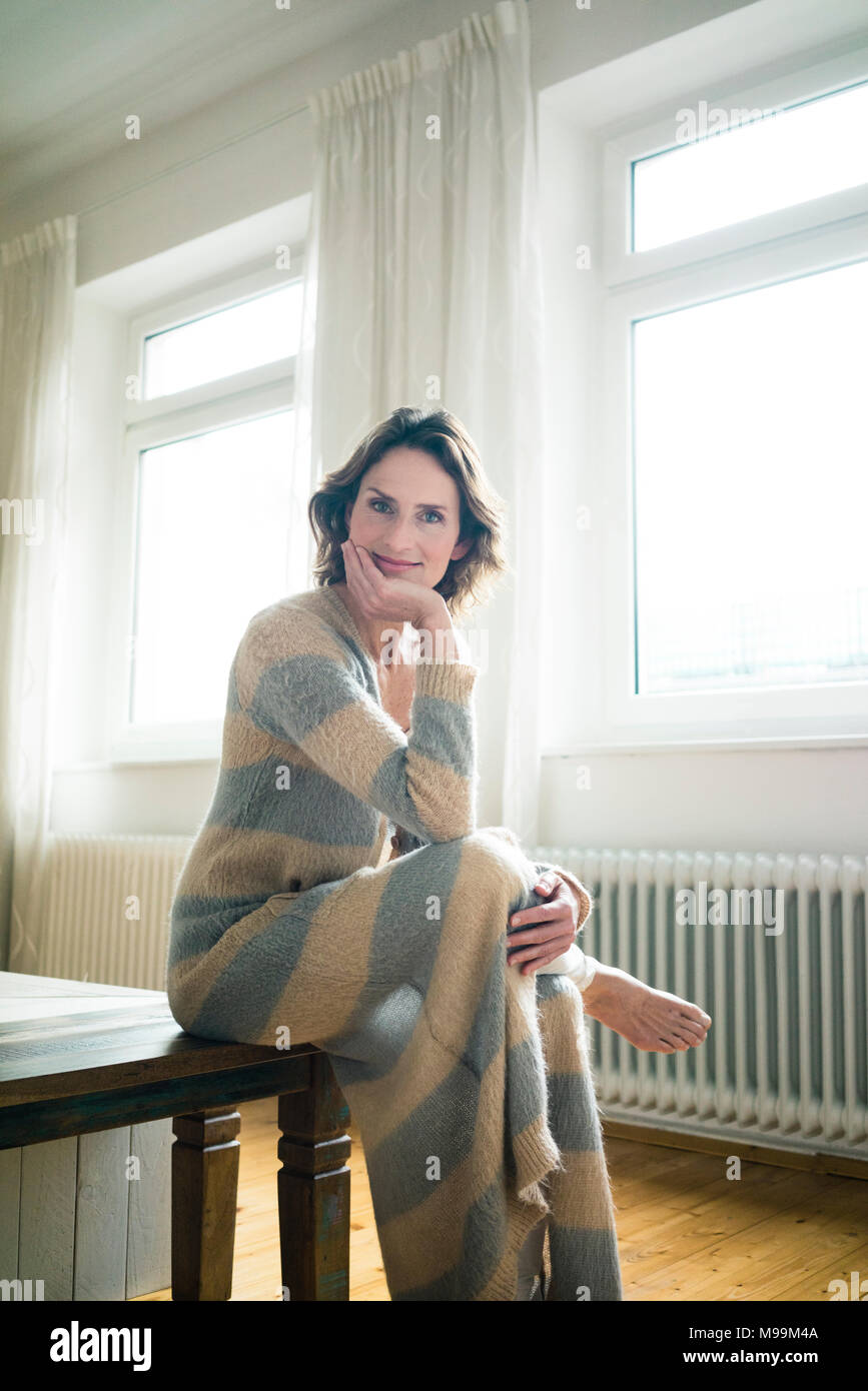 Portrait of smiling mature woman sitting sur banc en bois à la maison Banque D'Images