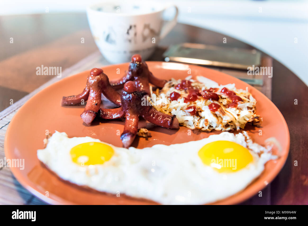 Petit-déjeuner brunch gros gros plan de la plaque avec les œufs, les pommes de terre Rissolées pommes râpé, ketchup, saucisses tako poulpe, tasse de café, téléphone smartphone Banque D'Images