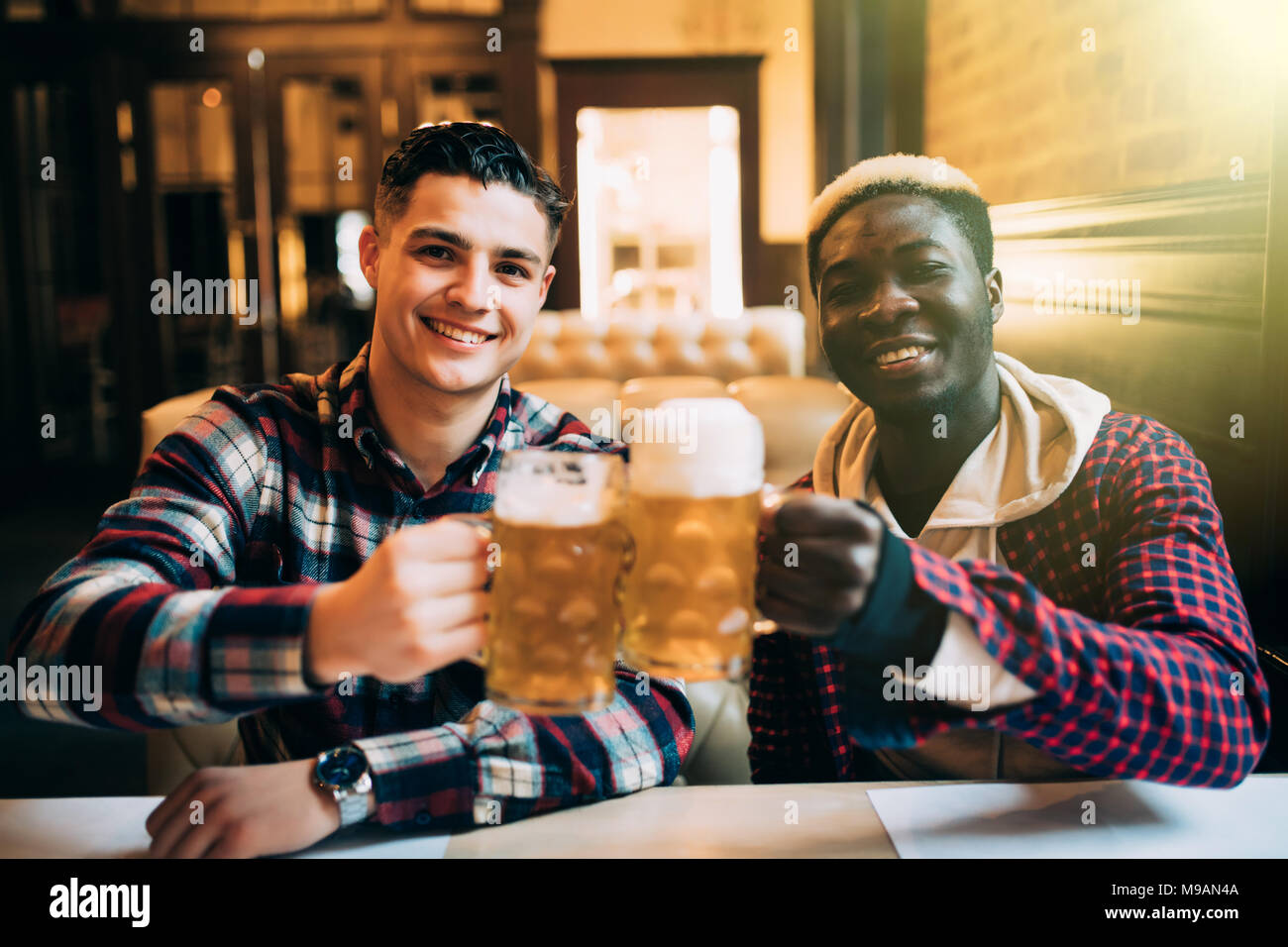 Deux meilleurs amis ou camarades de collège ayant la bière dans un pub. Homme African parle à son ami de race blanche, looking at camera Banque D'Images