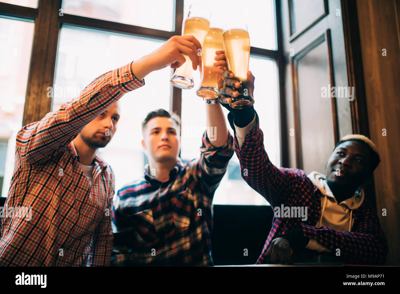Les hommes amis multiraciale cheers avec de la bière dans des verres dans un pub. Banque D'Images