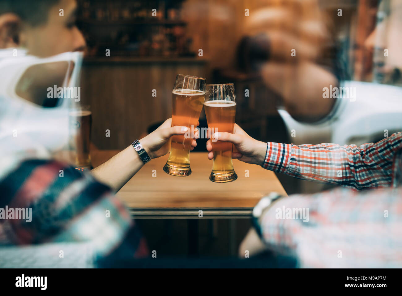 Close up amis assis au pub cheers avec verres de bières à travers la fenêtre. Banque D'Images
