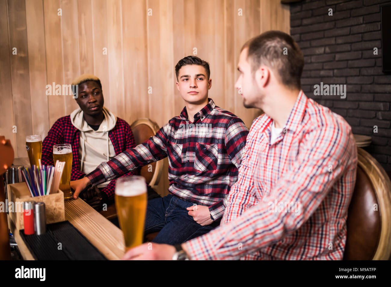Les amis s'est réuni après une dure journée. Trois joyeux ami clink bière au bar et boire une bière. Banque D'Images