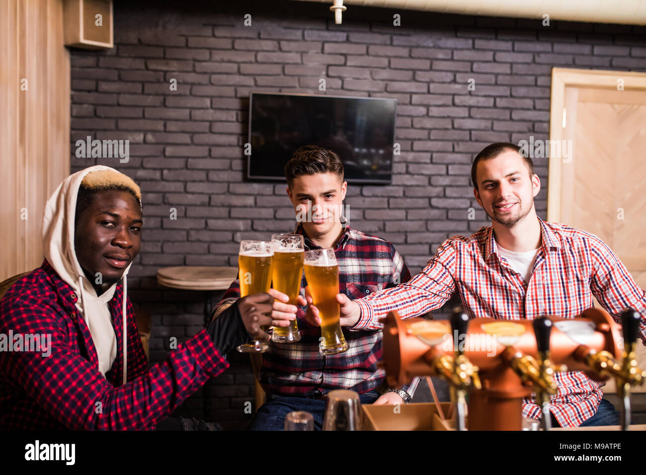 Beaux mecs sont clinking verres de bière et souriant tout en vous reposant à pub Banque D'Images