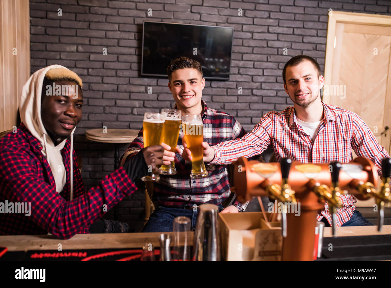 Beaux mecs sont clinking verres de bière et souriant tout en vous reposant à pub Banque D'Images