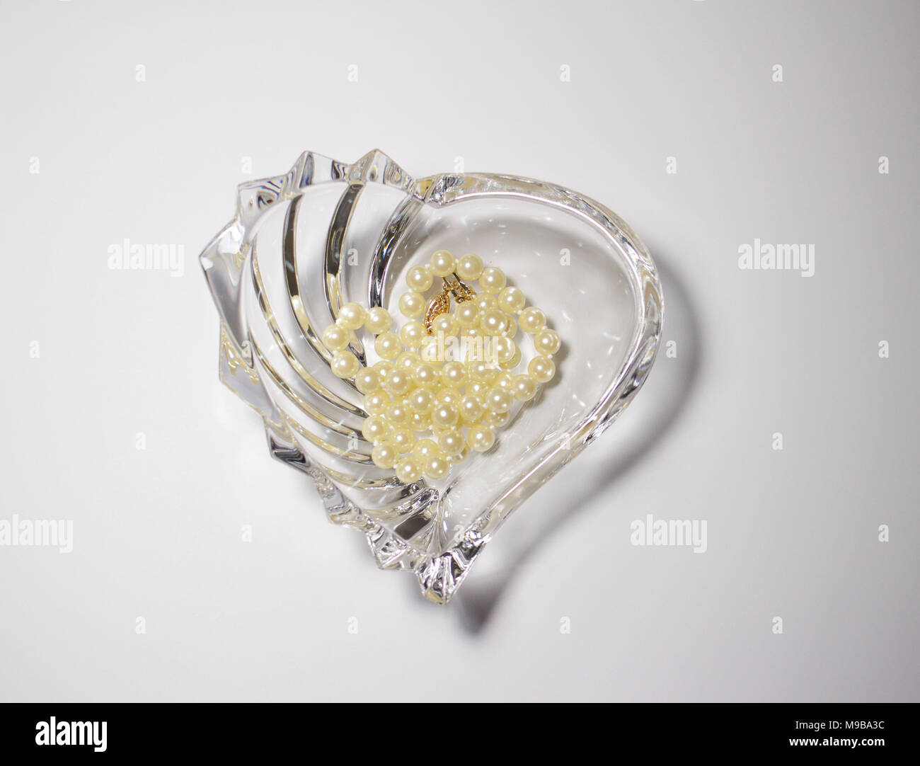 Vue rapprochée d'un établissement moderne en forme d'coeur cristal de plomb bol en verre contenant des perles perles de culture avec un fond blanc Banque D'Images