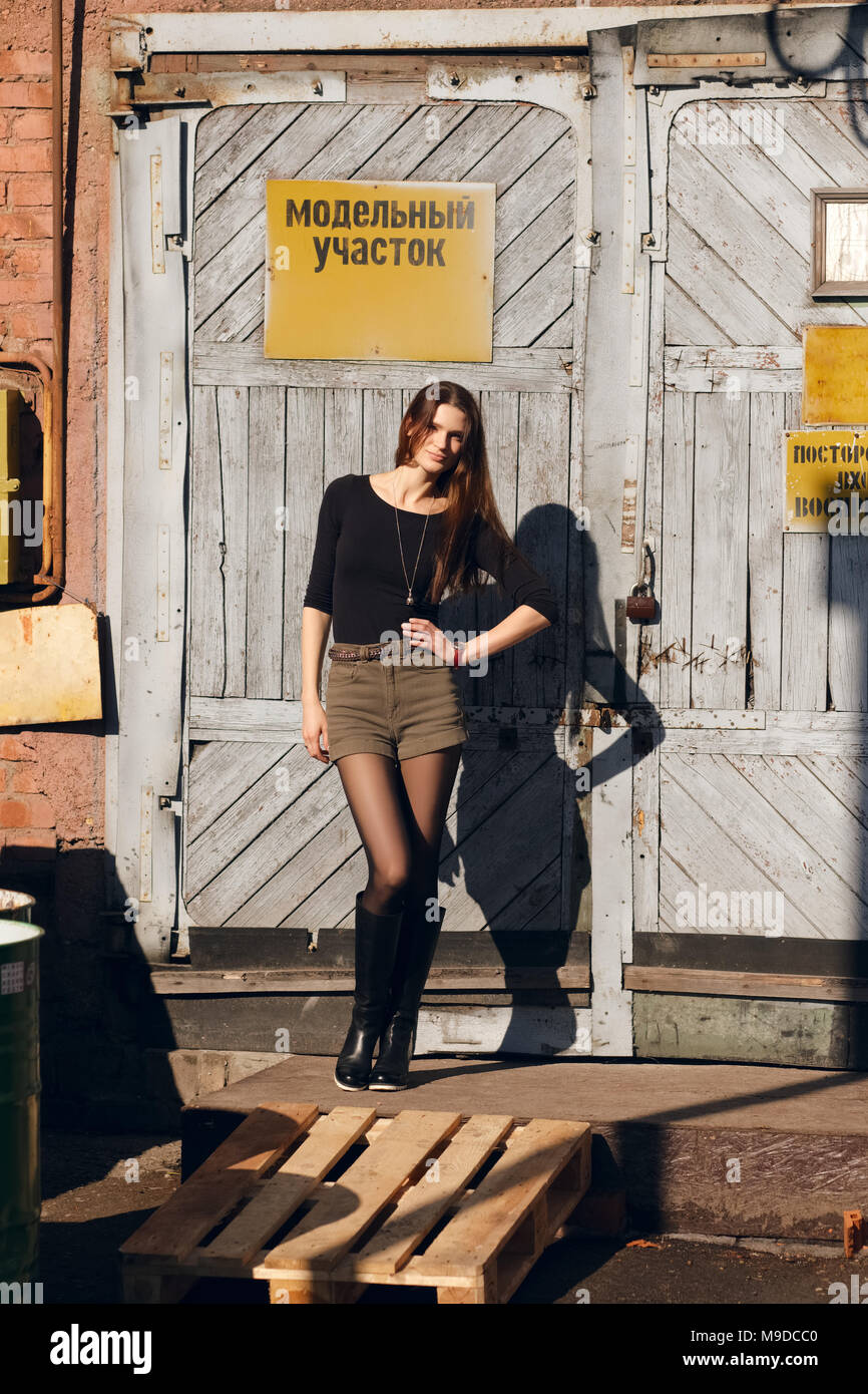 Jolie jeune fille posant devant la porte de l'usine avec plaque d'avertissement. (Inscription sur plaque est sur le russe peut être traduit comme région modèle et ne pas ent Banque D'Images