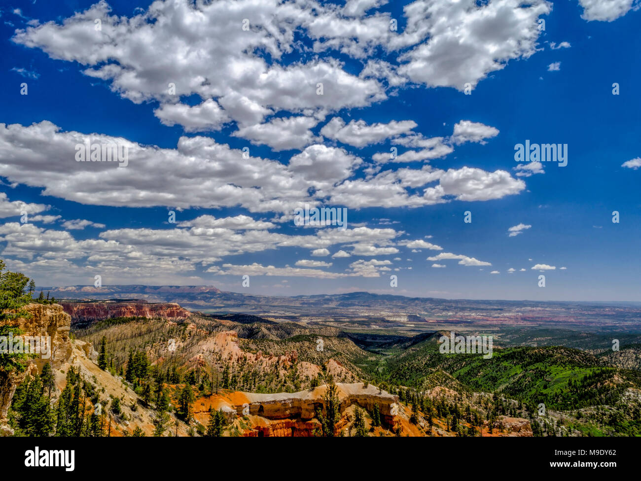 Donnant sur une vallée avec orange et rouge coteaux et falaises avec green valley ci-dessous sous un ciel bleu avec des nuages blancs moelleux. Banque D'Images