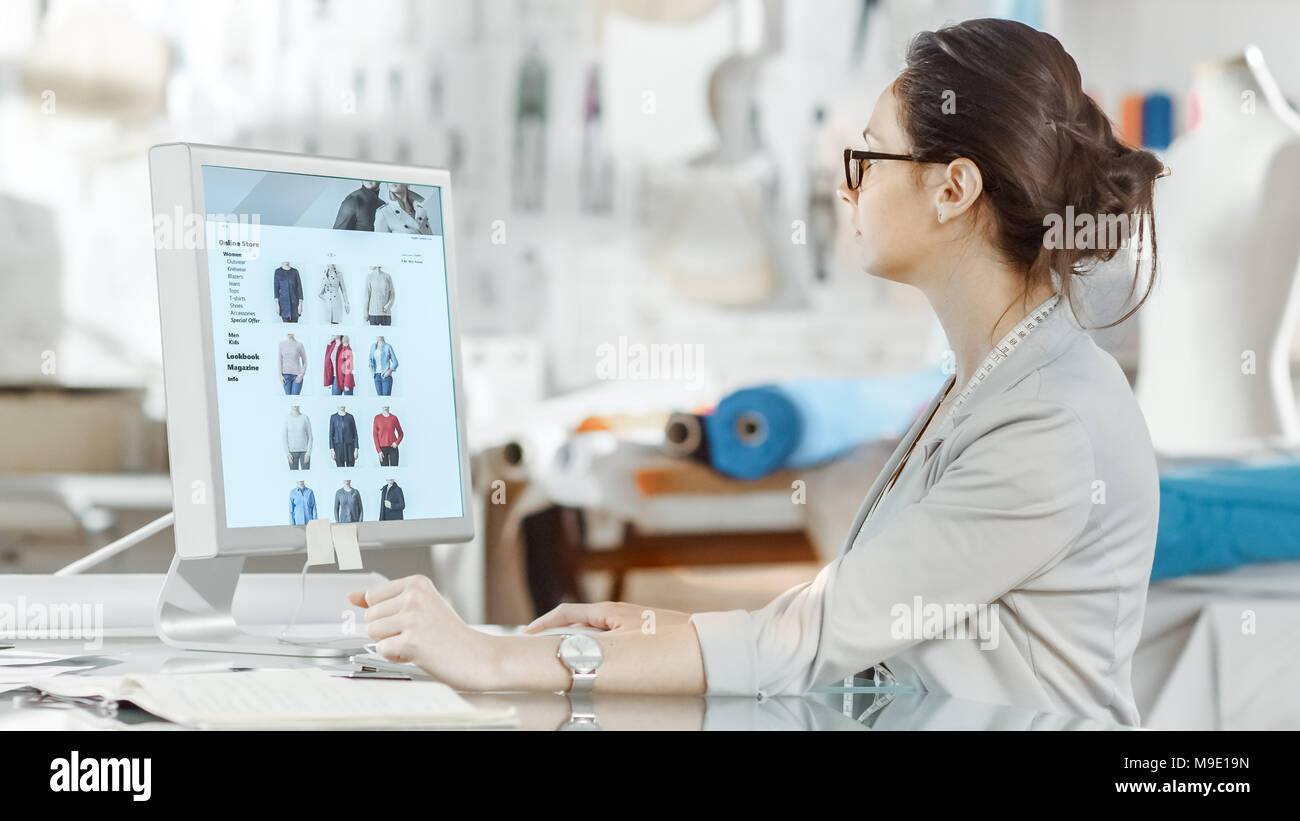 Beau la mode, designer, est assis à son bureau travaillant sur des croquis sur son ordinateur personnel. Son studio est ensoleillée, pleine de détails colorés, Tissus Banque D'Images