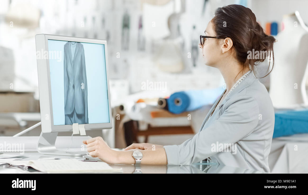 Beau la mode, designer, est assis à son bureau travaillant sur des croquis sur son ordinateur personnel. Son studio est ensoleillée, pleine de détails colorés, Tissus Banque D'Images