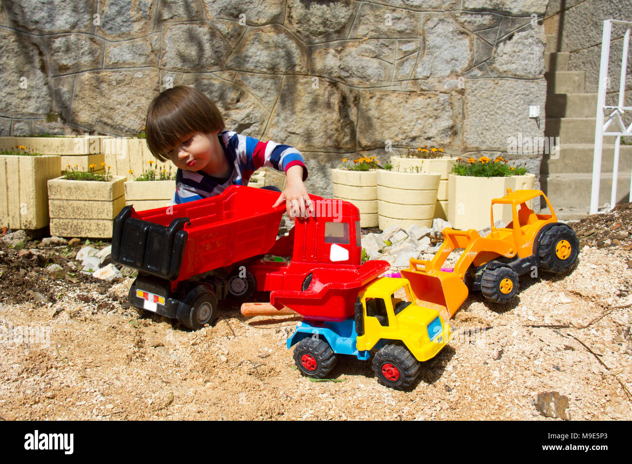 Petit garçon de trois ans jouant dans le sable avec une pelle et camion. Banque D'Images