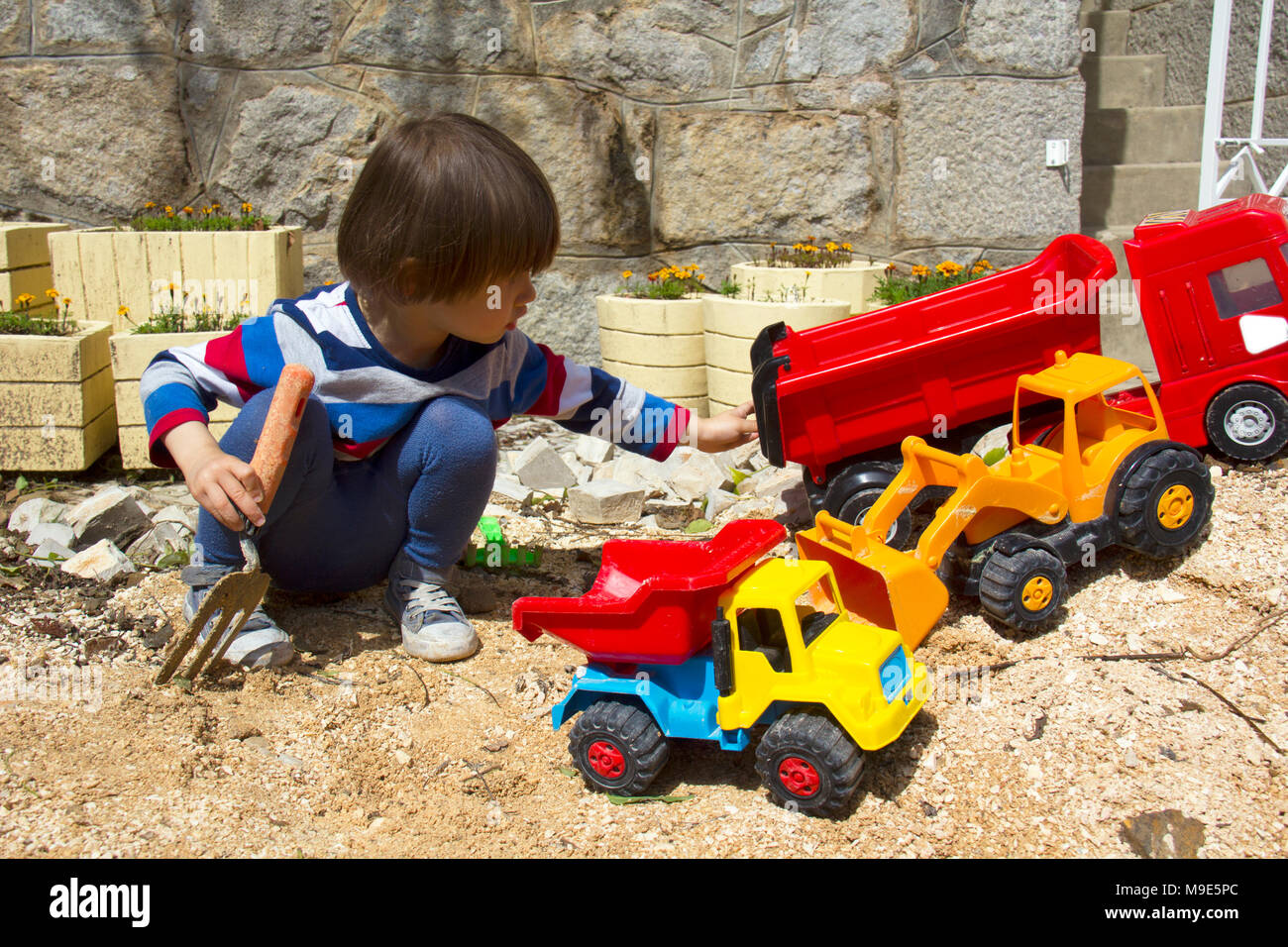 Petit garçon de trois ans jouant dans le sable avec une pelle et camion. Banque D'Images