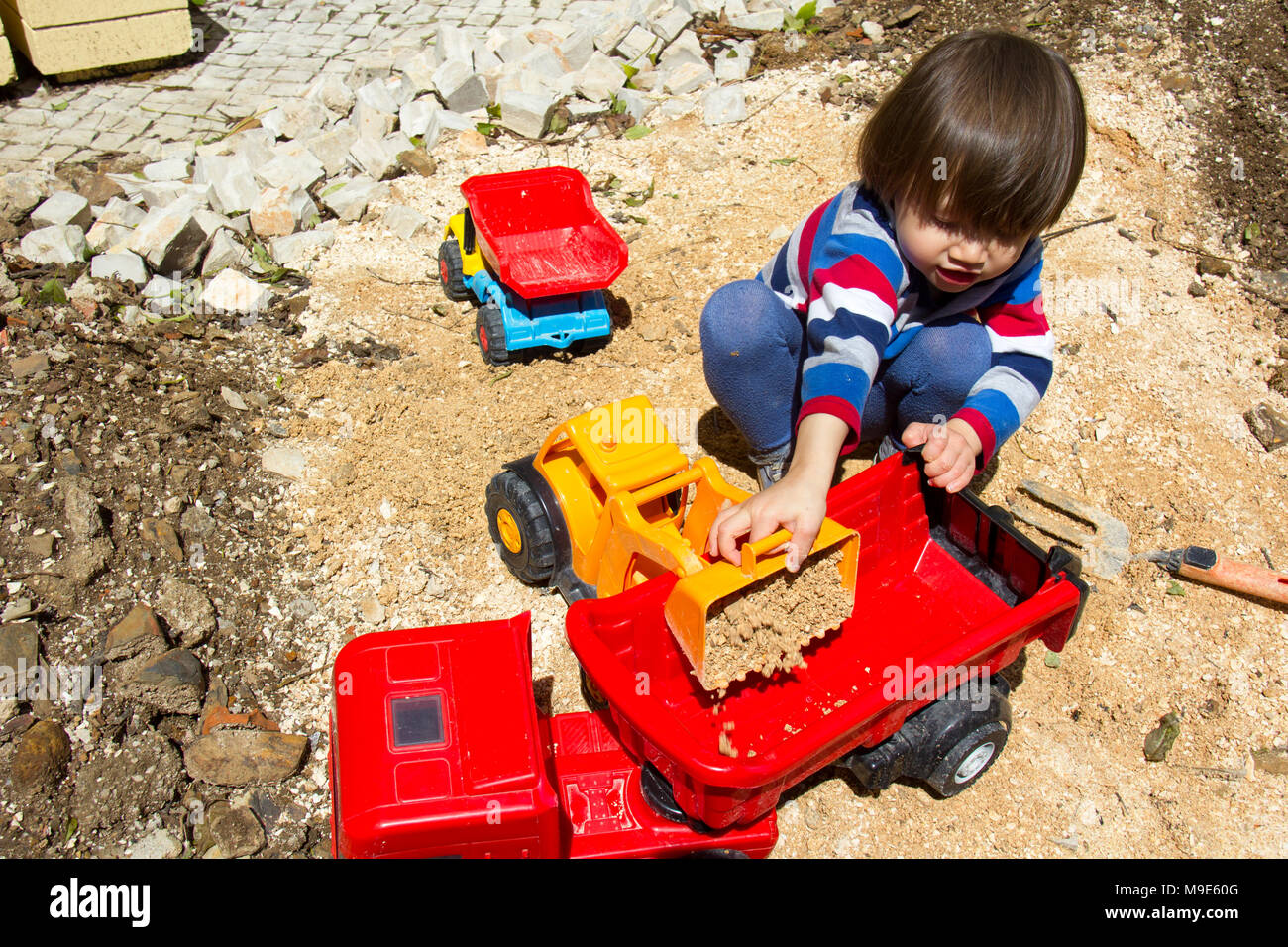 Petit garçon de trois ans jouant dans le sable avec une pelle et camion. Banque D'Images
