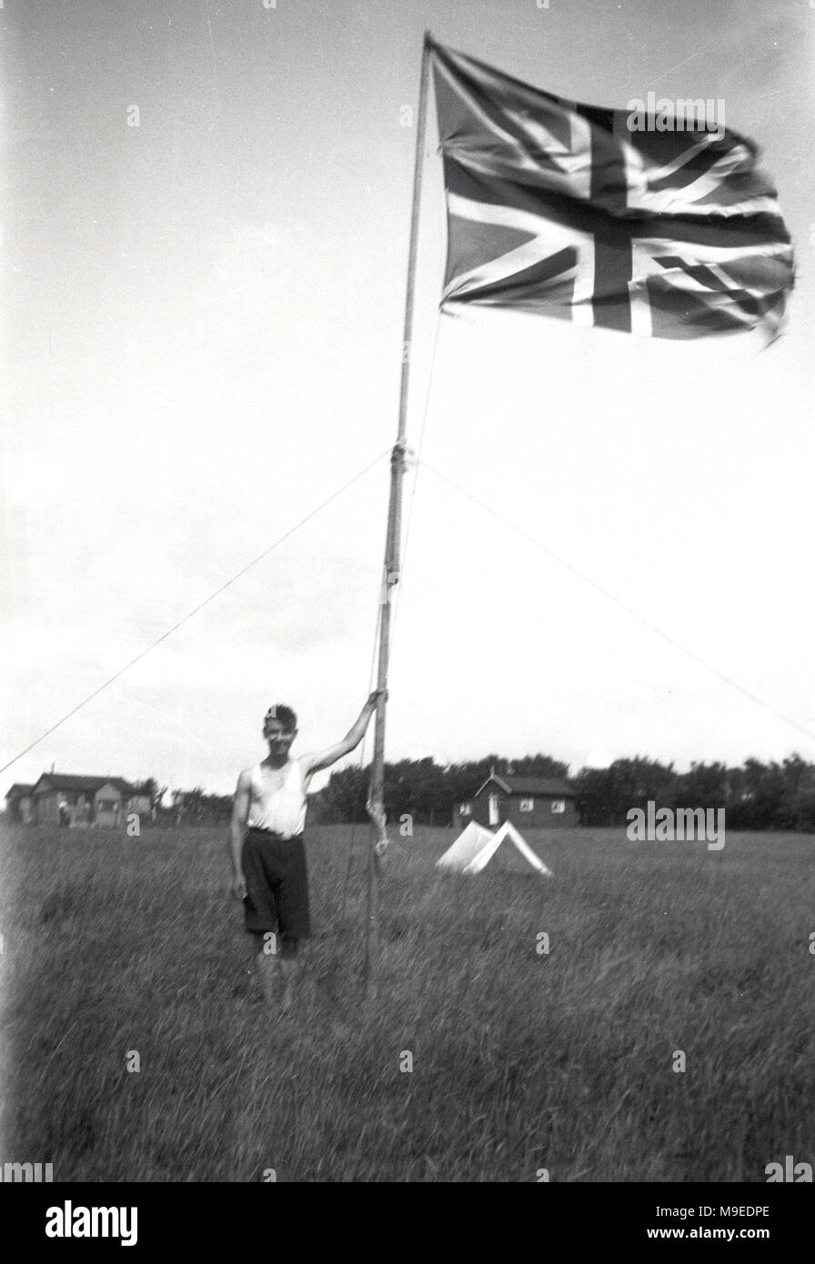 1934, historique, un jeune scout dans les champs à un camp scout à Dublin, Irlande, se dresse à côté de poudly de hauteur mât tenant une Union Jack flag/ Banque D'Images