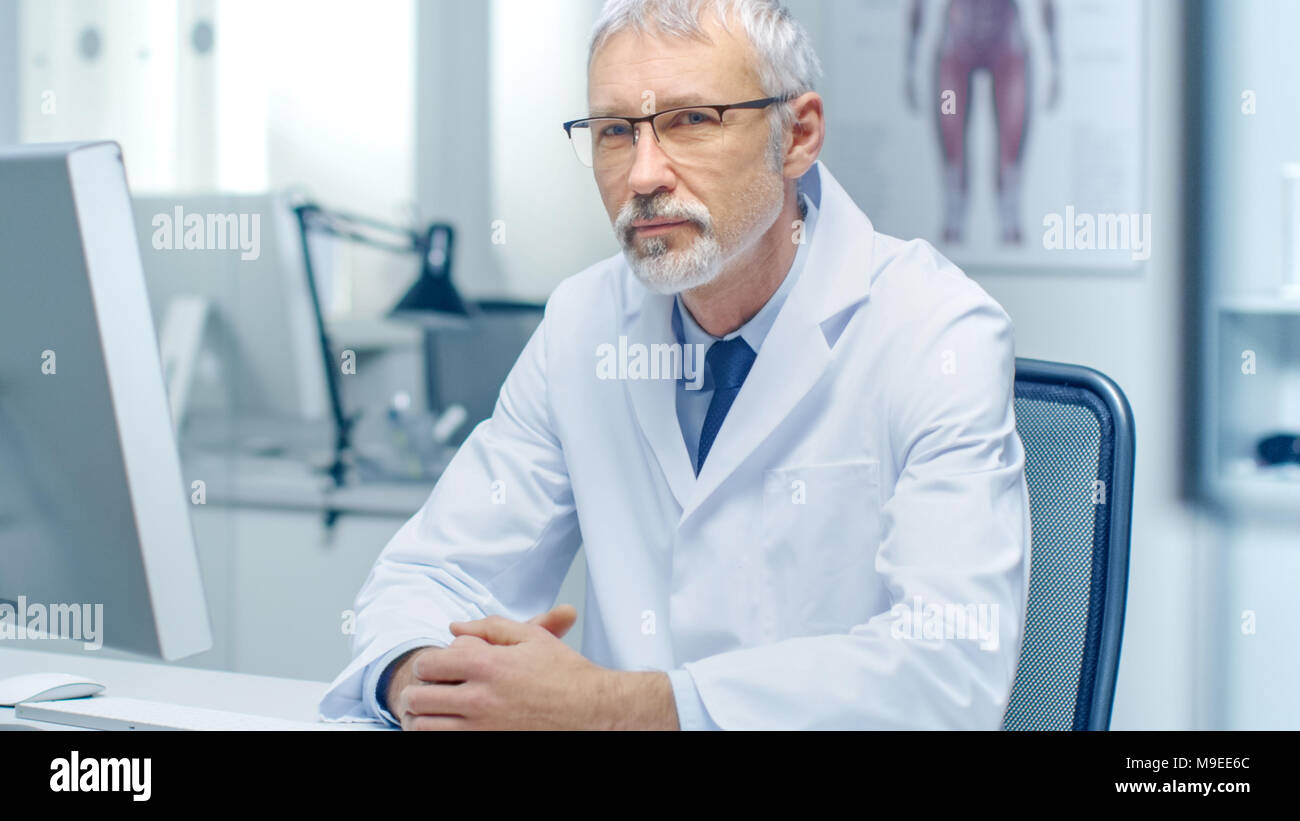 Aux cheveux gris expérimenté médecin senior à la recherche en appareil photo. Portrait en lumière moderne et bureau. Banque D'Images
