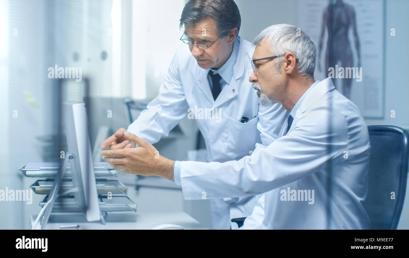 Deux postes de médecins à discuter de problèmes d'ordre médical sur ordinateur de bureau. Bureau est moderne et lumineux. Banque D'Images