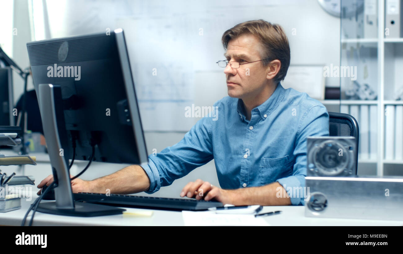 Bureau d'ingénierie d'occupation. Ingénieur en chef à son bureau de travail, certains éléments techniques se trouvant sur son bureau. Son assistant travaille à son bureau. Banque D'Images