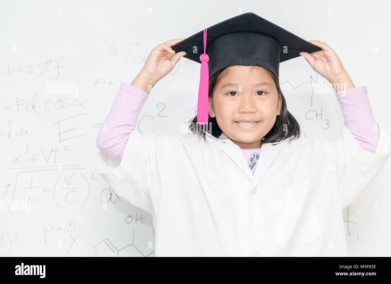 Cute asian girl scientifique porter graduation hat sourire sur inscription blanche avec l'équation scientifique, de la science et de l'éducation préscolaire concept Banque D'Images