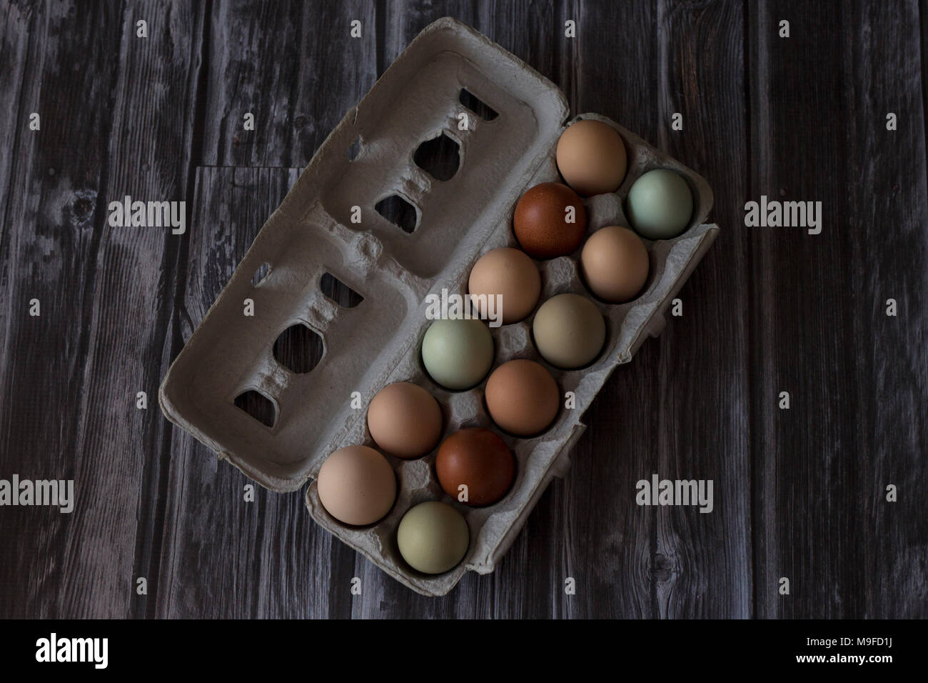 Un carton d'une douzaine d'oeufs frais de la ferme en plusieurs couleurs, sur un fond de bois Banque D'Images