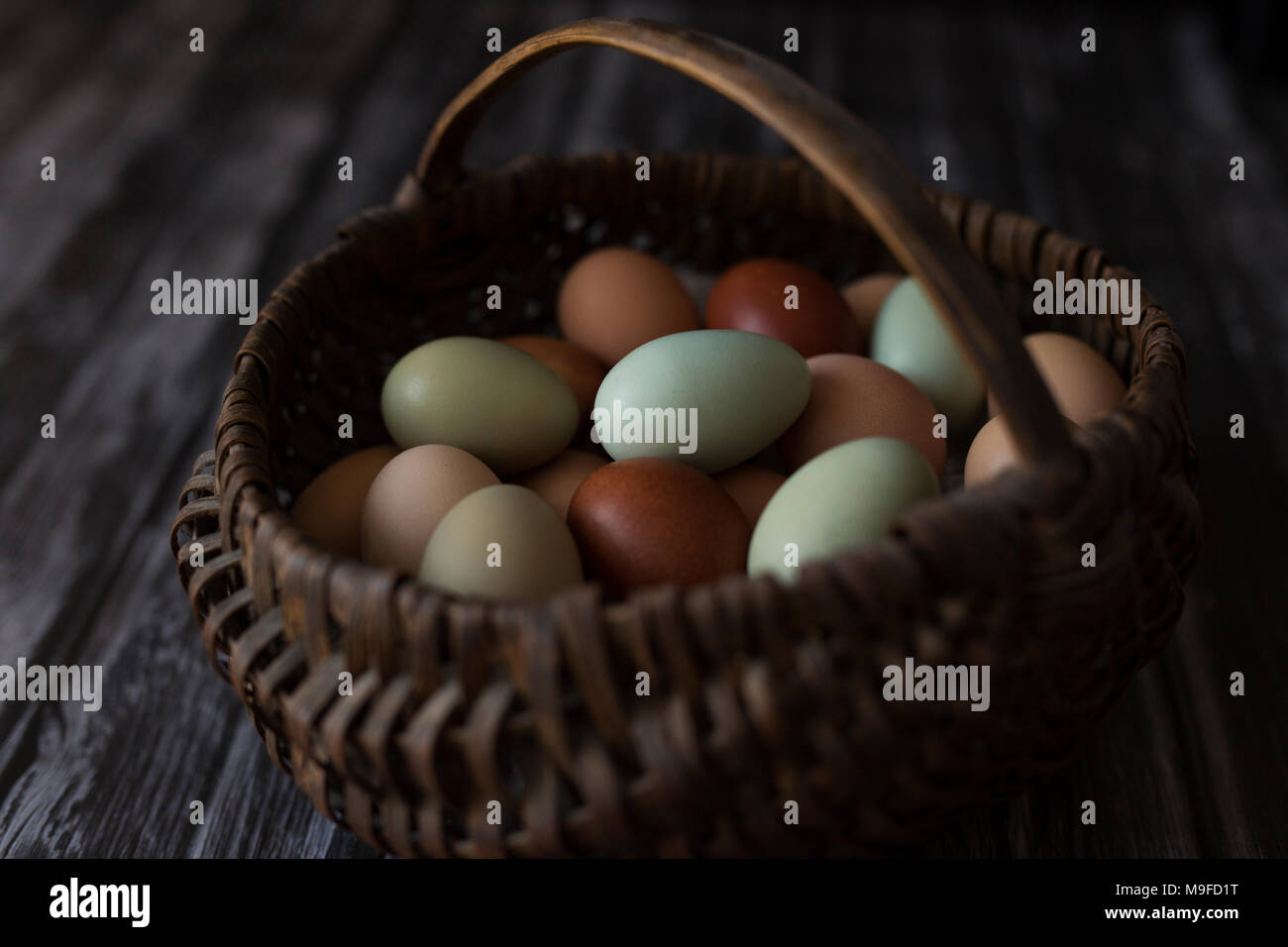 Un panier d'oeufs frais de la ferme en plusieurs couleurs, sur un fond de bois Banque D'Images