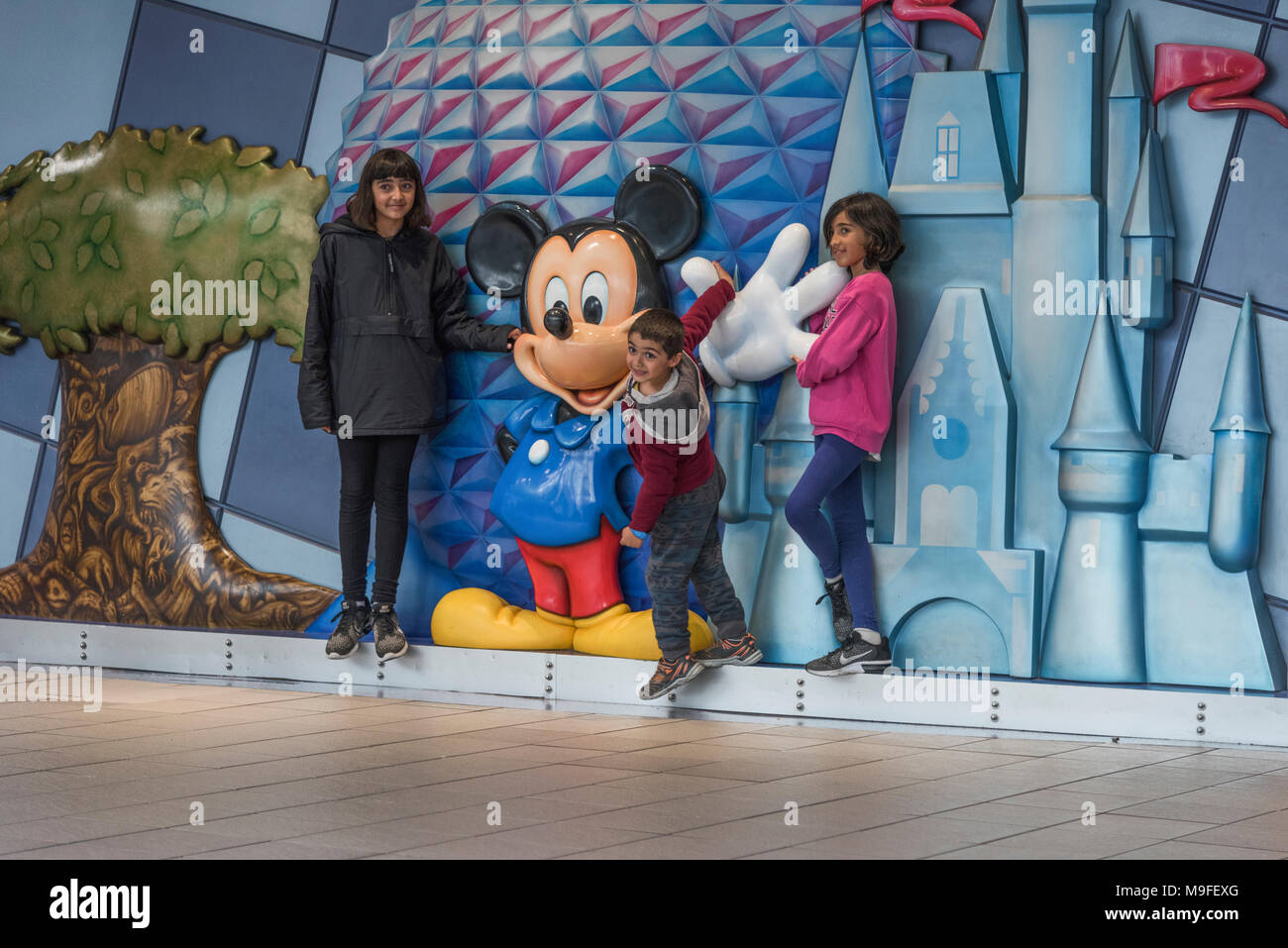 Les enfants posant avec un Micky Mouse statue situé dans l'aérogare à l'Aéroport International d'Orlando en Floride USA. Banque D'Images